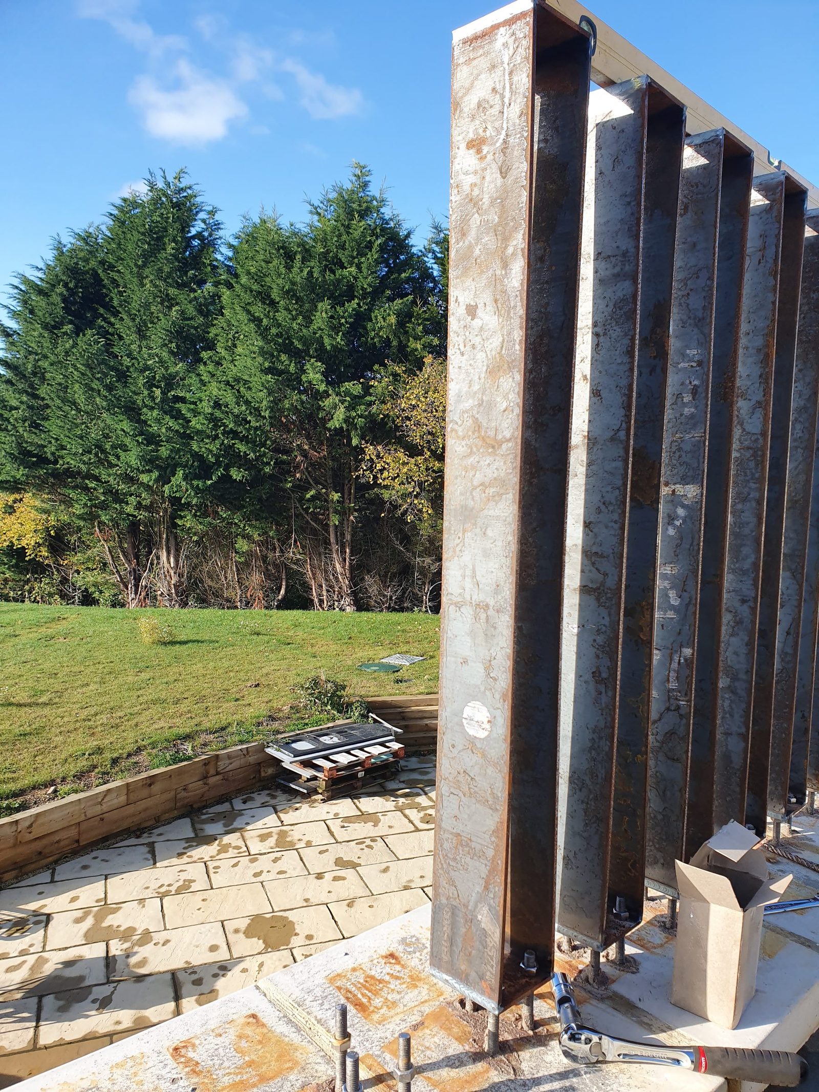 First upright corten posts installed beside a terrace wall.