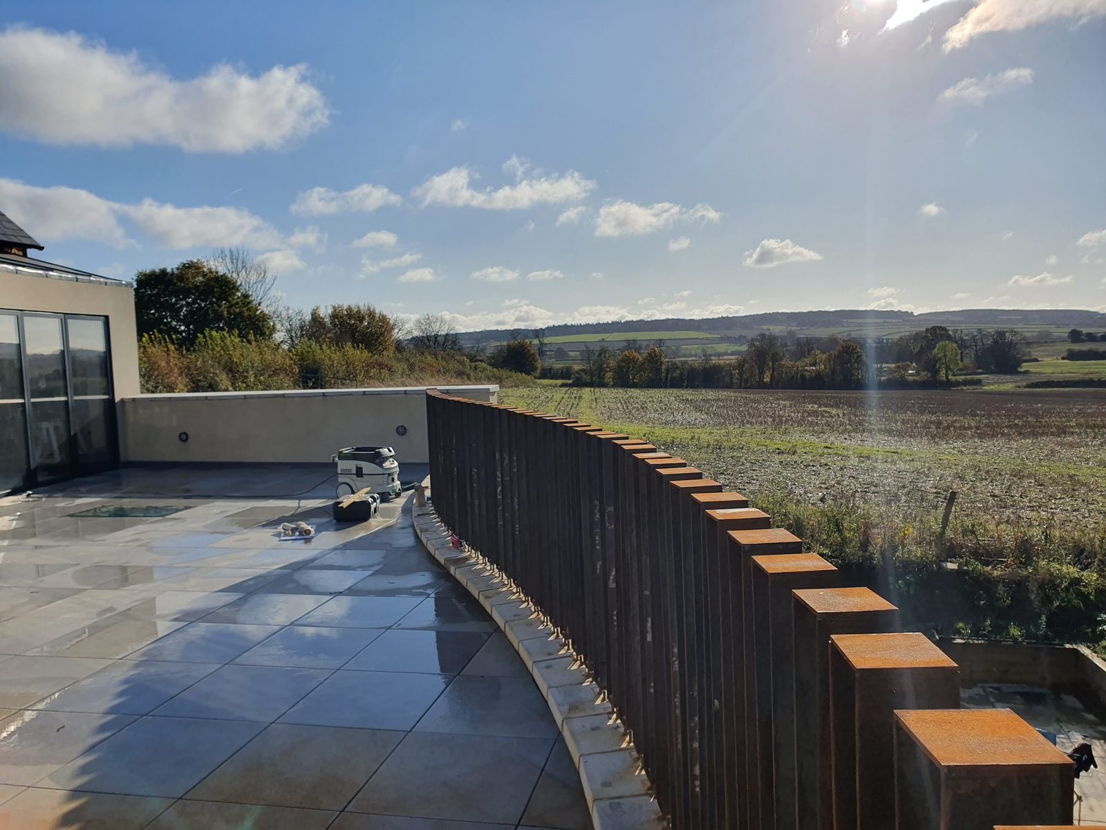 A curved weathering-steel balustrade on a terrace overlooking fields.