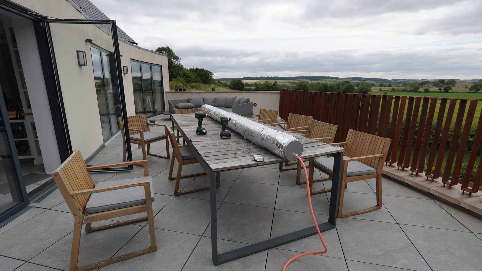 A long foil-wrapped steam box on a terrace beside a curved balustrade and countryside view.