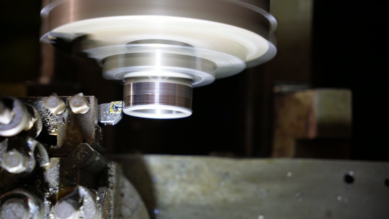 A pale spinning workpiece on the lathe as sparks begin to gather behind the tool.