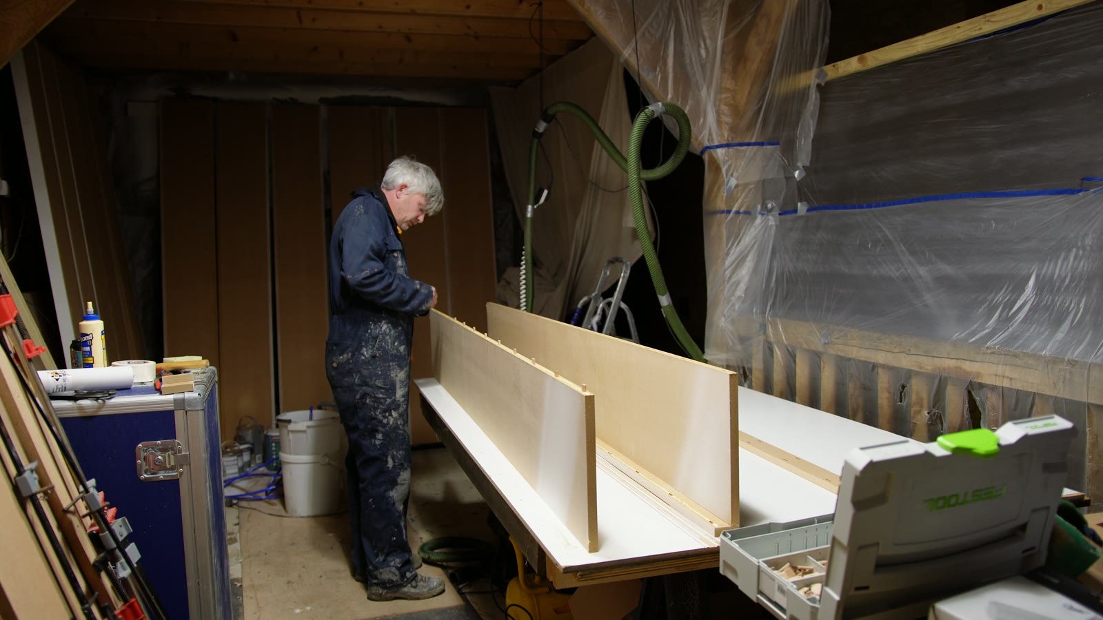 Daniel assembling pale cabinet sections on a long workbench.