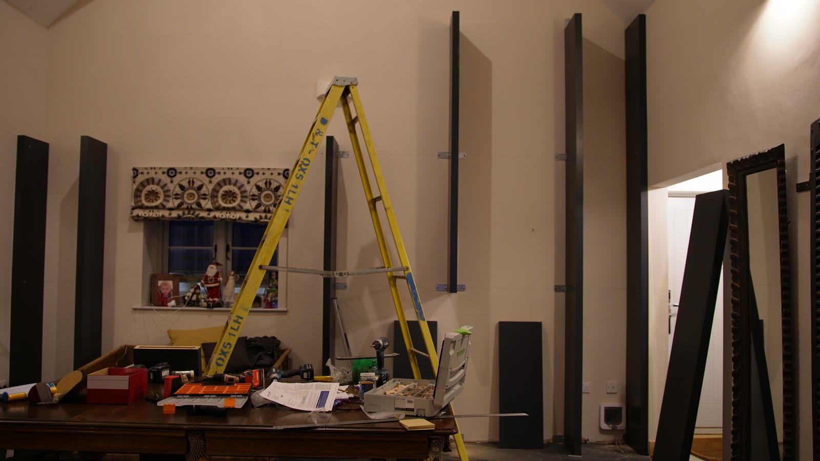 Tall dark bookcase uprights and a yellow ladder during fitting in the room.