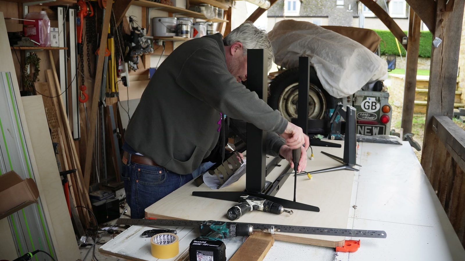 Daniel assembling the black motorised desk frame on a large work table.