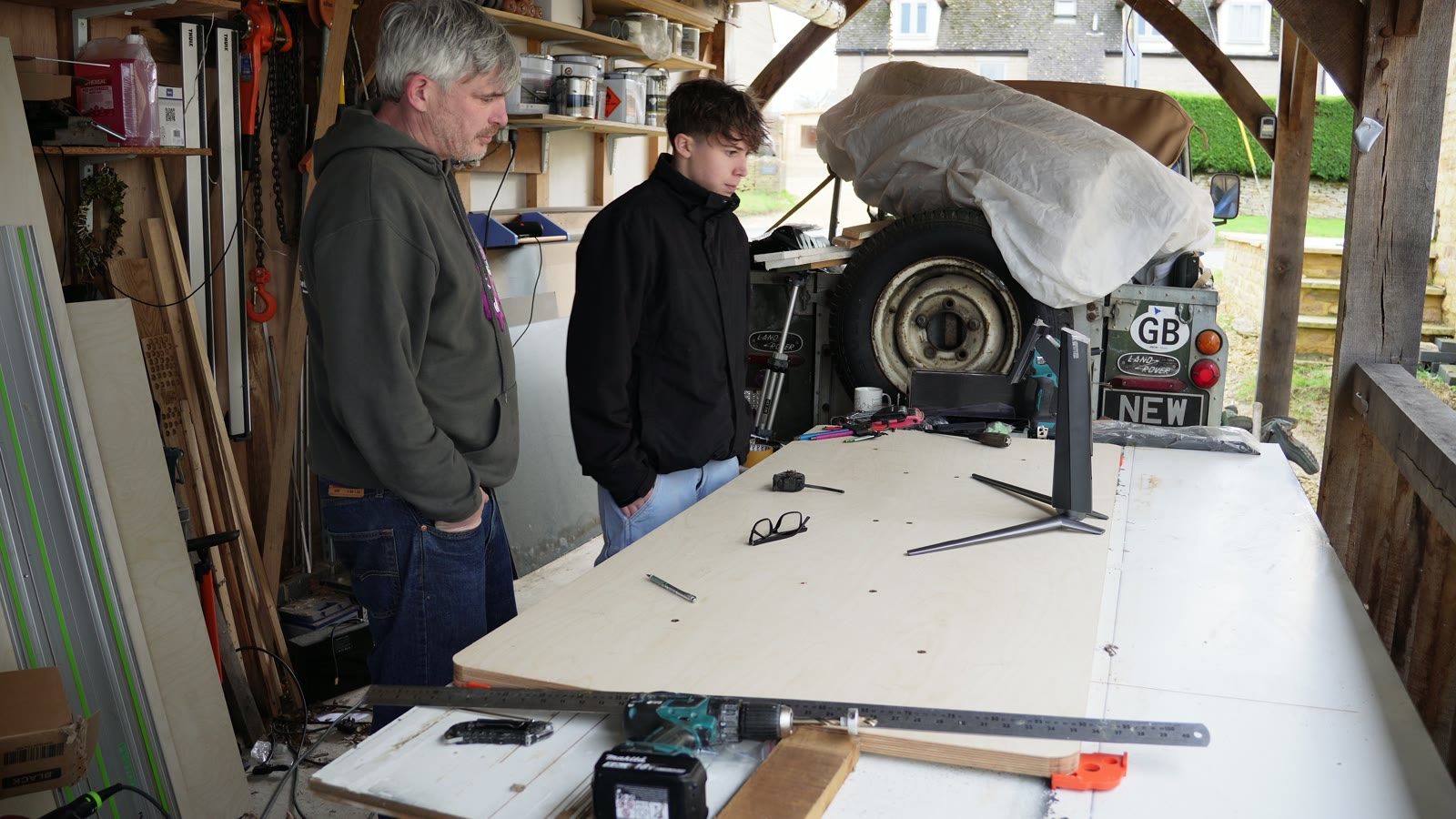 A black motorised desk frame and pale tabletop being assembled on a workshop bench.