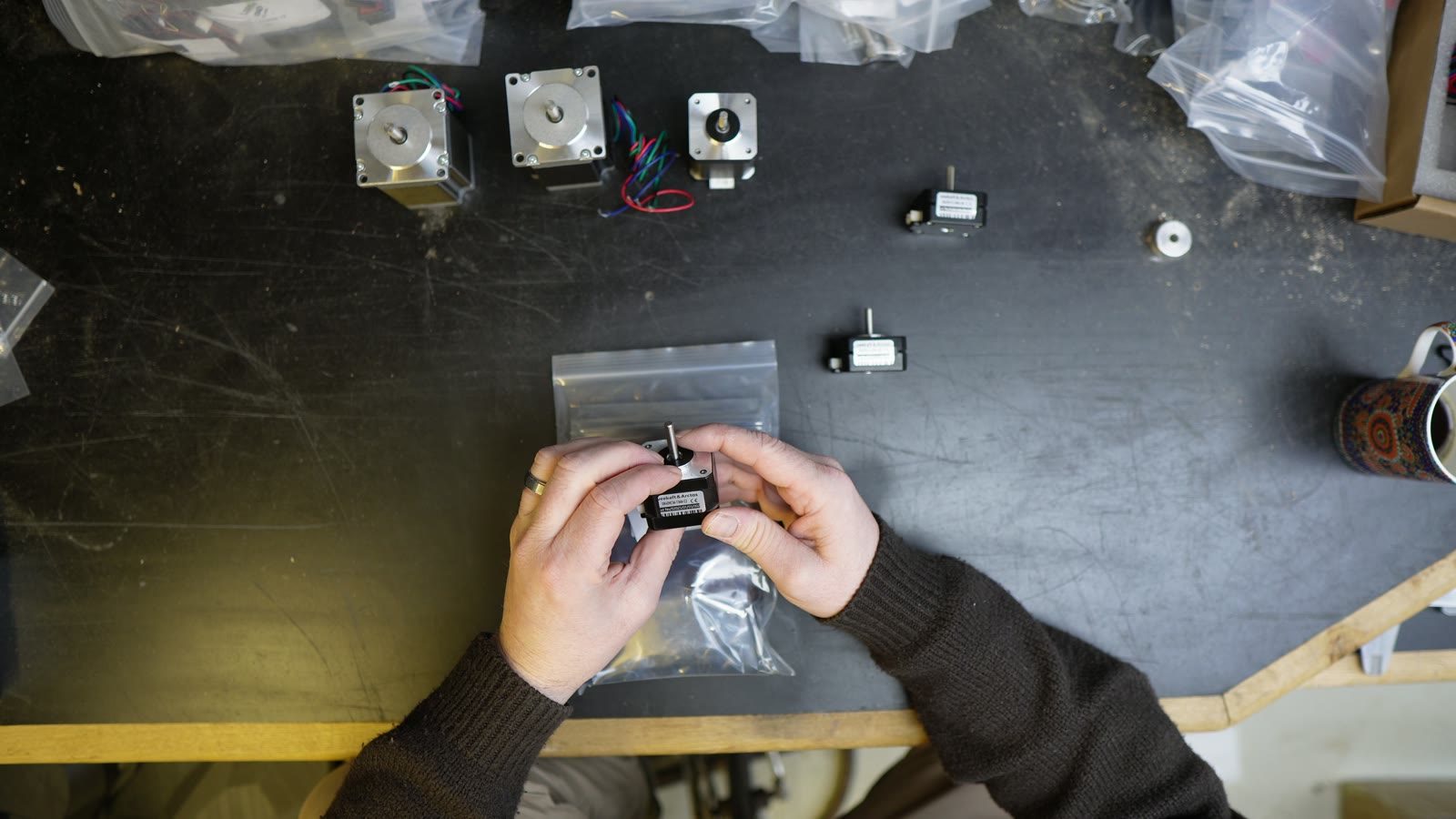 Hands assembling or testing a robot arm servo component on the bench.