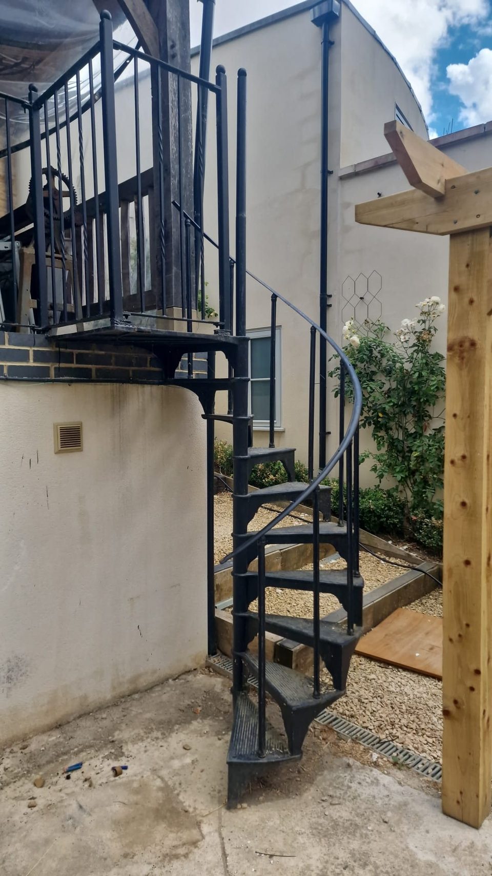 Finished black spiral staircase installed beside a house and timber pergola.