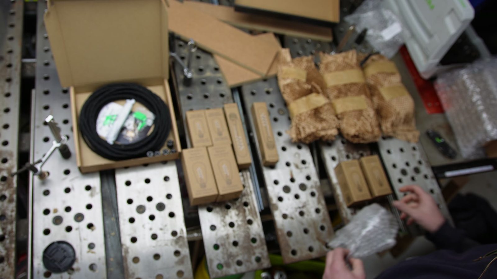 Lighting parts, cable and wooden pieces laid out on a welding table.