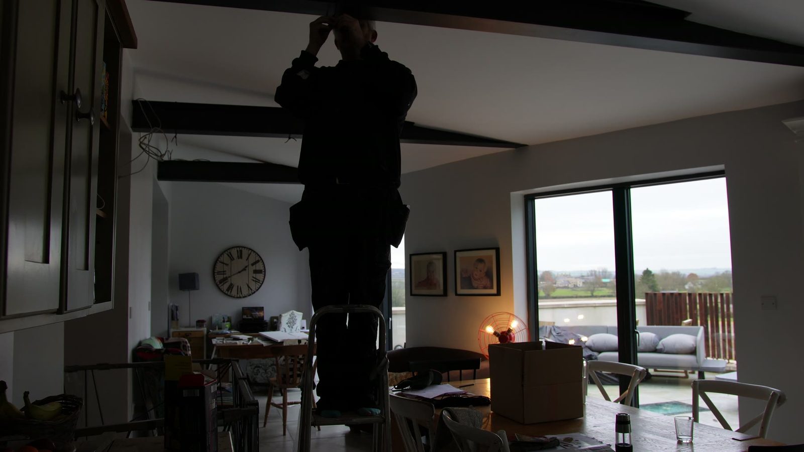 Daniel installing string lights across dark ceiling beams.