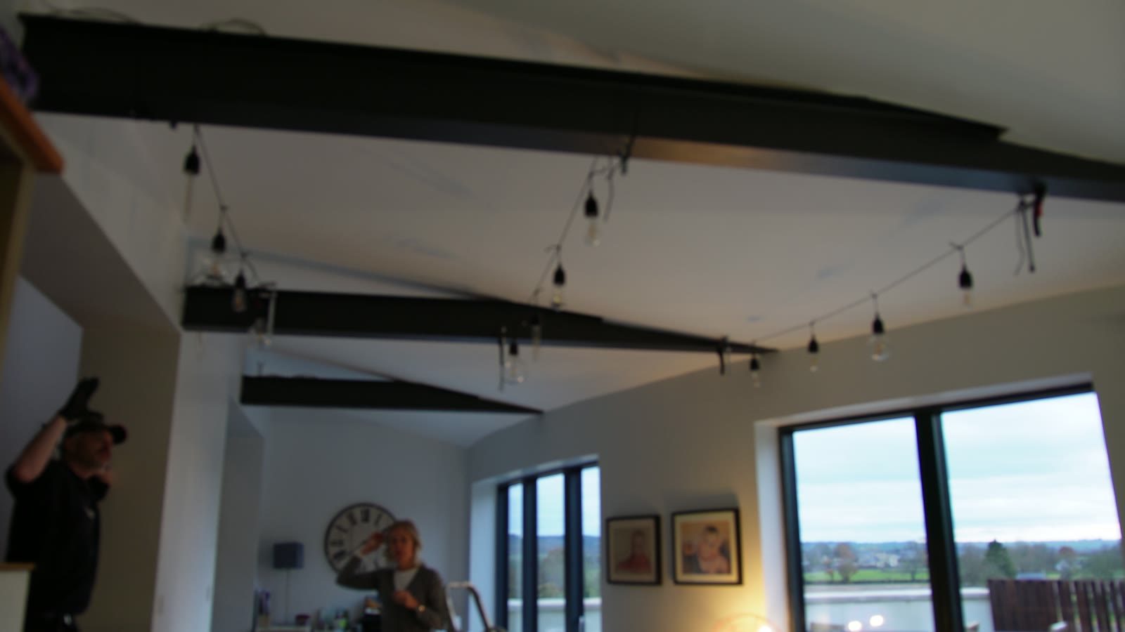 Vintage string lights installed across dark beams in the finished room.